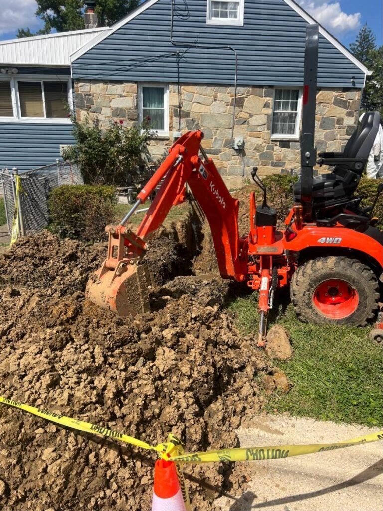 Mini excavator trenching for a new water line beside a stone house